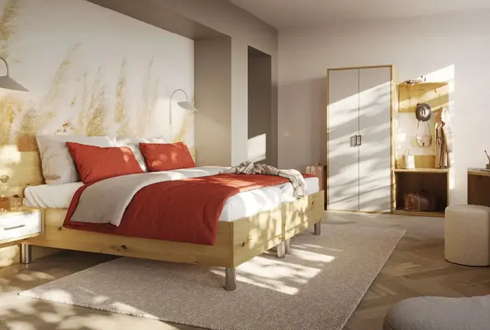 Schlafzimmer mit Holzbett und rot weisser Bettwäsche auf hellem Teppich, links Nachttische mit Lampen, rechts Kleiderschrank und offene Garderobe aus Holz.